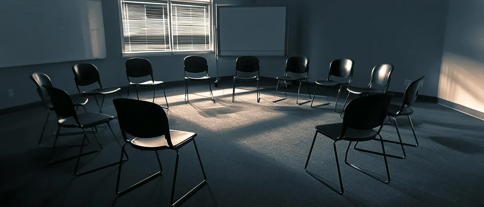 A circle of black chairs in an empty room, morning light coming through the blinds